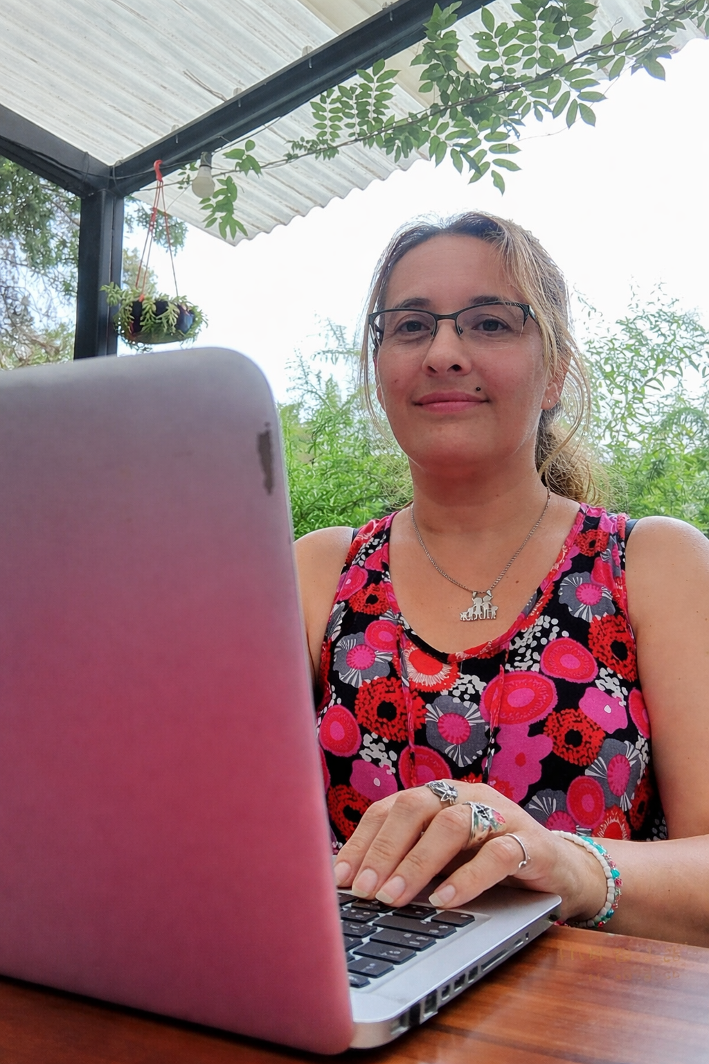 Mujer emprendedora sonriendo frente a una laptop con un mate, en un estudio ordenado con plantas.