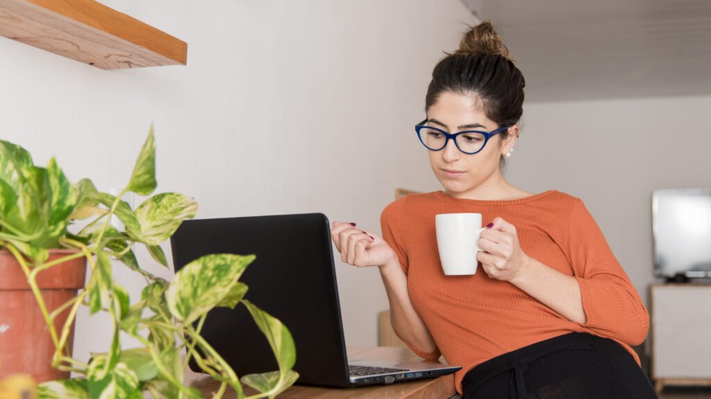 Mujer emprendedora sonriendo frente a una laptop con un mate, en un estudio ordenado con plantas. arte de delegar para recuperar tu vida y potenciar tu marca